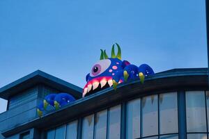 Colorful monster sculpture on building rooftop against twilight sky, whimsical urban art concept in Manchester, England. photo