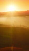 Silhouettes of mountains and village locating among them. Stunning rocky landscape in the bright orange light of setting sun. Vertical video