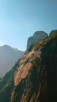 Picturesque rock of Yosemite National Park, California, USA. Beautiful mountain with some trees growing on top. Clear sky at backdrop. Vertical video