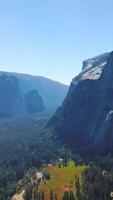 Sunlit pine tree forest surrounded by powerful rocks. National Park of Yosemite, California, USA from aerial view. Vertical video