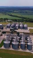 Enormous agricultural granary complex in the farmlands. Aerial view. Green fields and forests at the background. Vertical video