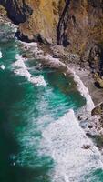 Aquamarine waters of Pacific Ocean meeting rugged craggy rocks of the California coast. Amazing white waves at Morro Bay from aerial view. Vertical video