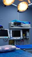 Equipment with screens near the operational table prepared for surgery. Multiple varied apparatuses piled at the wall of the ward. Vertical video