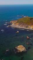 Rocky beach covered with moss, lichen and few bushes. Amazing coastline of Pacific at Morro Bay, California, USA. Aerial view. Vertical video