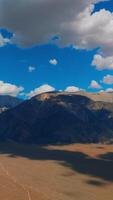 sbalorditivo montagne nel il ombre di bianca soffice nuvole. Nevada rocce a fondale di azzurro cieli con morbido nuvole. verticale video
