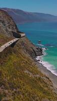 zweispurig Autobahn mit Tunnel auf das Berge von Kalifornien Küste. schön Aussicht von azurblau Ozean beim das Ufer. oben Sicht. Vertikale Video