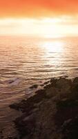 Fantastisk orange solnedgång över de pacific hav. skön hus byggd mycket stänga till de klippig Strand av kalifornien kustlinjen. vertikal video