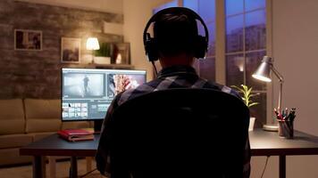 Back view of videographer editing a movie using post production software in home office at night. video