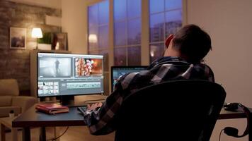 Back view of content creator talking on the phone while editing a movie in home office at night. video