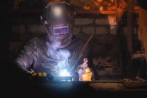 Village workshop, welding in an old garage. An unrecognizable man repairs a metal part wearing protective gloves and a mask photo