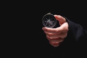 woman hand holds a compass showing south on a black background. A hand from the darkness holds out a compass, the concept of being lost and finding a solution or ideas with meanings photo