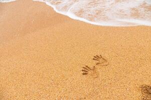 human traces of two hand prints on a sandy beach without people, sea waves rolling in from the side photo