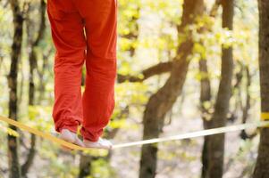 un hombre en naranja Deportes pantalones camina equilibrio en un tenso slackline de cerca foto