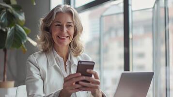 ai generado medio Envejecido caucásico negocio gerente CEO utilizando teléfono inteligente y ordenador portátil sonriente mujer de negocios participación teléfono inteligente sentar en oficina trabajando con Copiar espacio foto