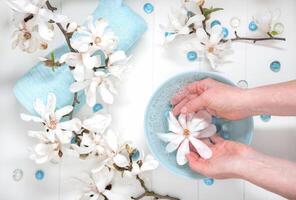 Hands of a young girl with natural manicure and a bowl of water with white magnolia flowers, spa treatments and massage photo