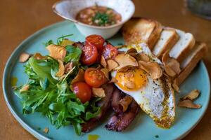 Fried eggs with bacon, tomatoes and arugula on a plate photo