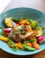 Fried fish with vegetables in a blue plate on a wooden table photo