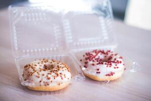 Donuts in a plastic box on a wooden table. Selective focus. photo
