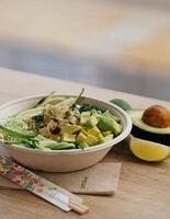 Bowl of avocado salad with tofu and cucumber on wooden table photo