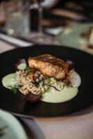 Risotto with salmon in a black plate on a restaurant table photo