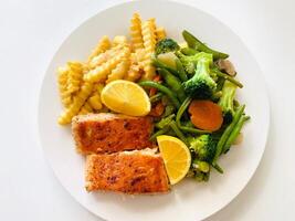 Grilled salmon with french fries and vegetables on a white plate. photo