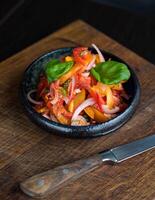 Tasty tomato salad with onion and basil in black bowl on wooden table photo