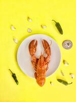 Boiled crayfish on a white plate with chili peppers and garlic on a yellow background photo