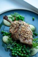 roasted duck leg with green peas and parsley on a plate photo