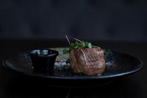 carne de vaca filete en un negro plato con salsa en un oscuro antecedentes foto