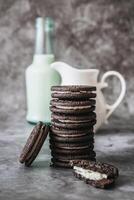 Chocolate cookies with cream filling and a bottle of milk on a gray background photo