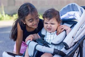 un pequeño hermana con su bebé chico hermano en un silla de ruedas foto