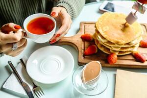Woman Holding a Cup of Tea and a Stack of Pancakes photo