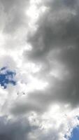 White and grey clouds forming in the blue sky. Rays of sun breaking through the clouds timelapse. View from below. Vertical video