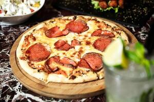 Pepperoni Pizza on Cutting Board With Drink photo