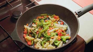 caucasian hand stirring vegetables in a frying pan with stainless steel fork while frying, close-up video