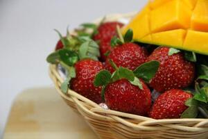 a basket of strawberries and mangoes on the cutting board on white background photo