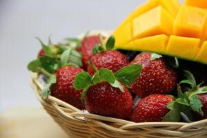 a basket of strawberries and mangoes on the cutting board on white background photo