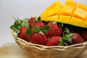 un cesta de fresas y mangos en el corte tablero en blanco antecedentes foto