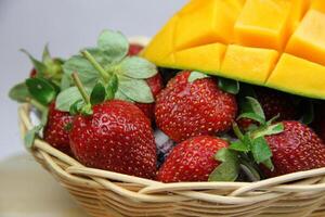 a basket of strawberries and mangoes on the cutting board on white background photo