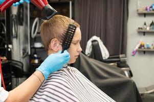 Boy at hair salon getting hairstyle with comb and blow dryer. photo