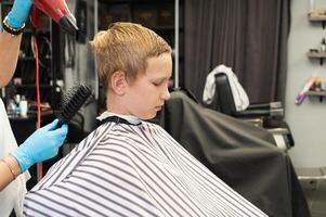 Young boy getting a haircut with hairdryer and brush at a barber shop. photo