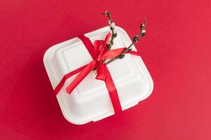 Closed gift box with willow branch on a red background. red gift ribbon photo