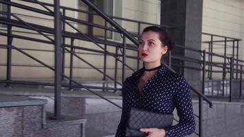 Portrait. Sexy business girl in a dark shirt and carrying a bag goes near the business center video