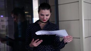 Beautiful business girl in dark clothes reading working papers standing near the building video