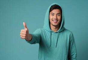 AI Generated A cheerful young man wearing a turquoise hoodie gestures a thumbs up, his bright expression evoking friendliness and enthusiasm. photo