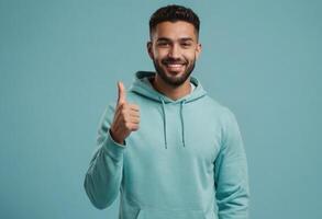 AI Generated A young man in a teal hoodie giving a thumbs up, his beard and bright smile conveying friendliness and casual style. photo