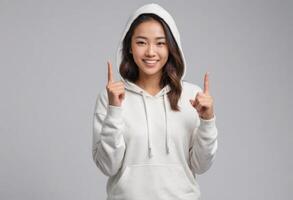 AI Generated An Asian woman in a white hoodie points upwards with both hands, showing enthusiasm and a bright smile. photo