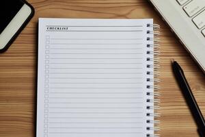 Blank checklist with space for ticks on notepad with laptop, smartphone and pen. photo