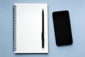 Smartphone with notebook and pen on blue background. Copy space. photo