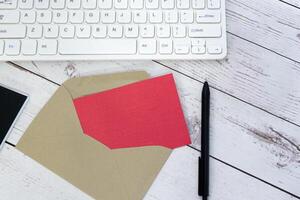 Red note inside brown envelope with keyboard on wooden desk. Copy space. photo